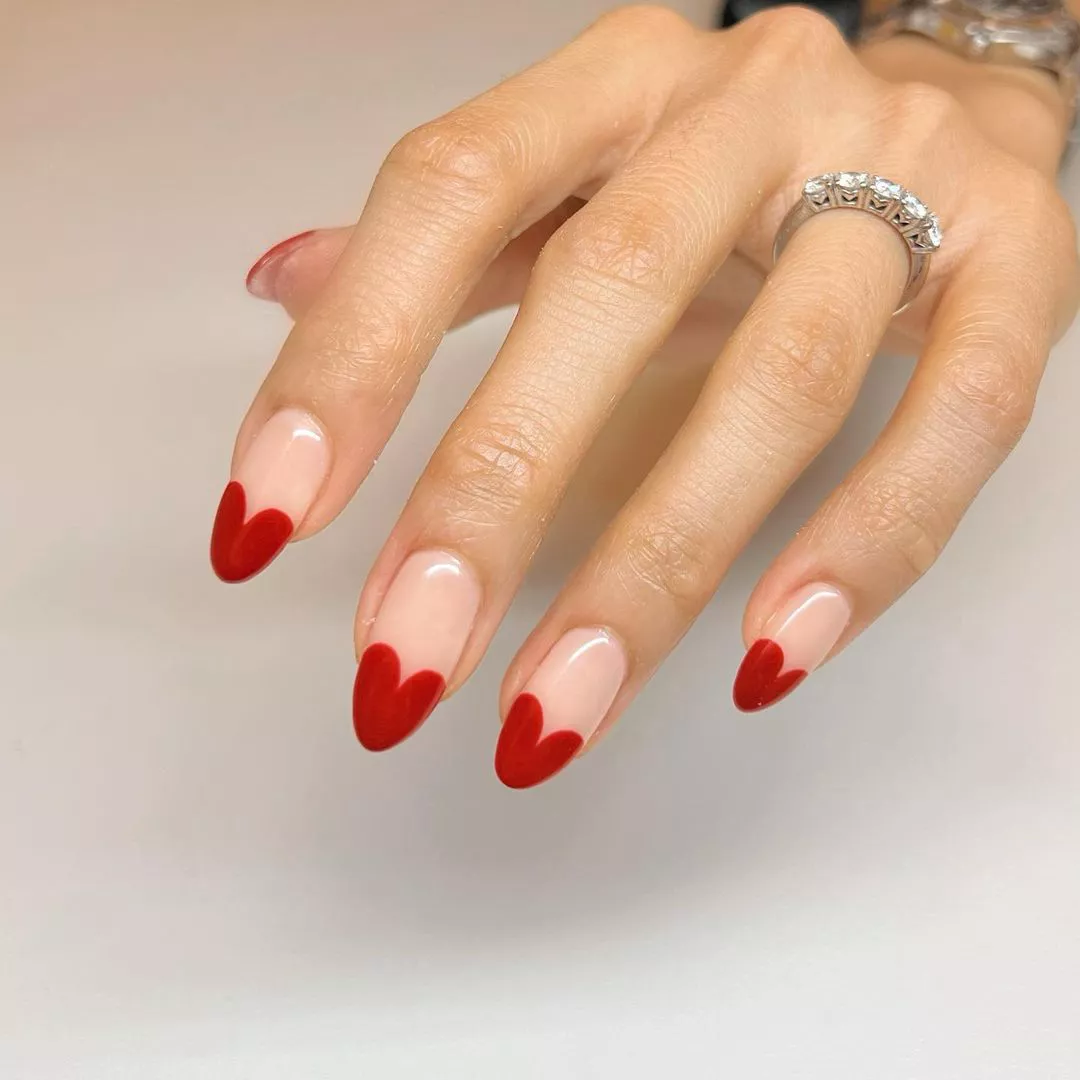 Person showing off their manicure, which has a neutral base and red heart French tips