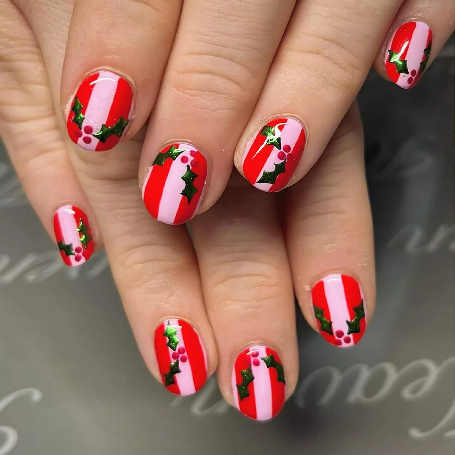 Person showing off their holiday-inspired red nails with green mistletoes and pink stripes