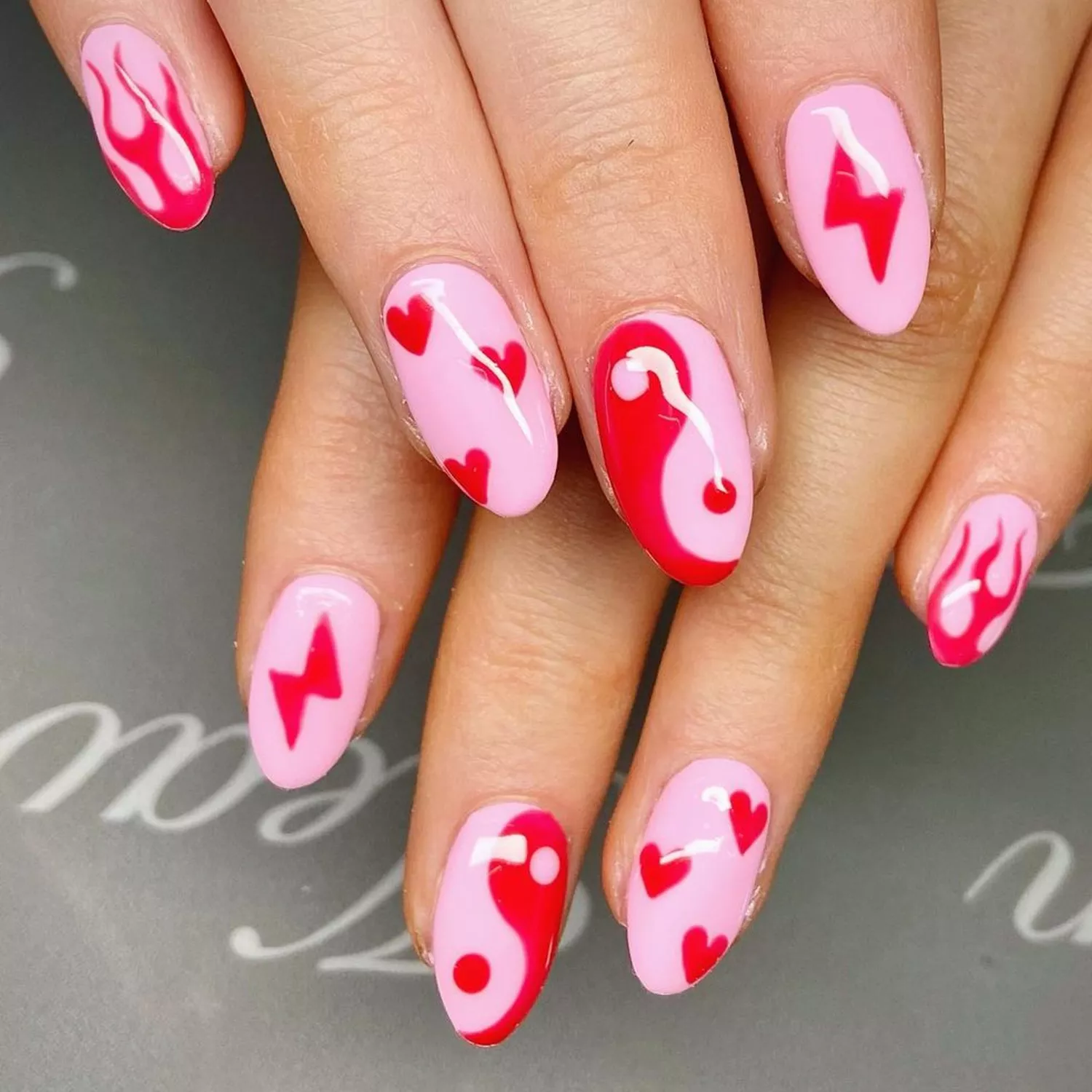 Pink and red mismatch nails with hearts, flames, and lightning bolts on individual fingers