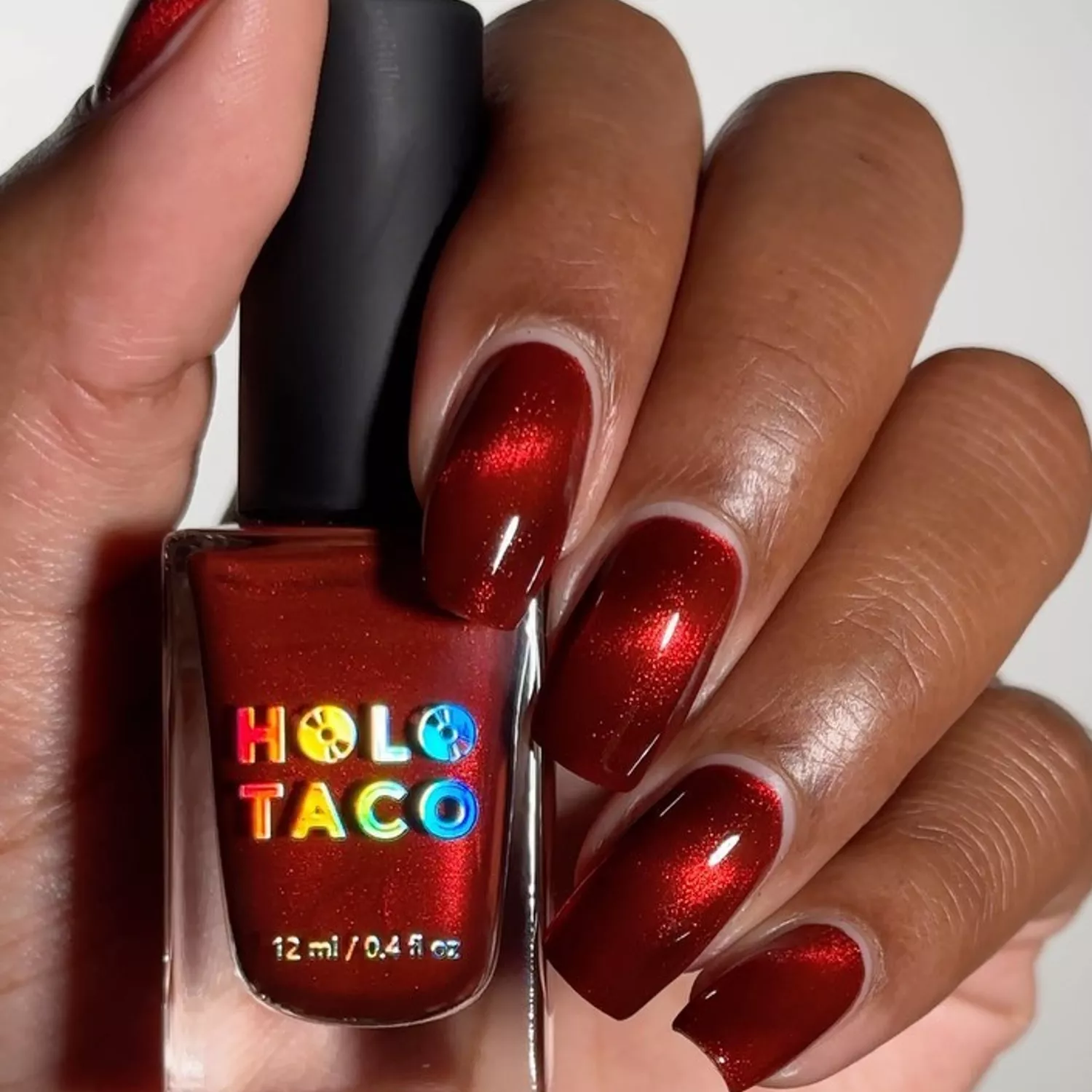 Person holding a dark red bottle of Holo Taco nail polish to show off their red nails