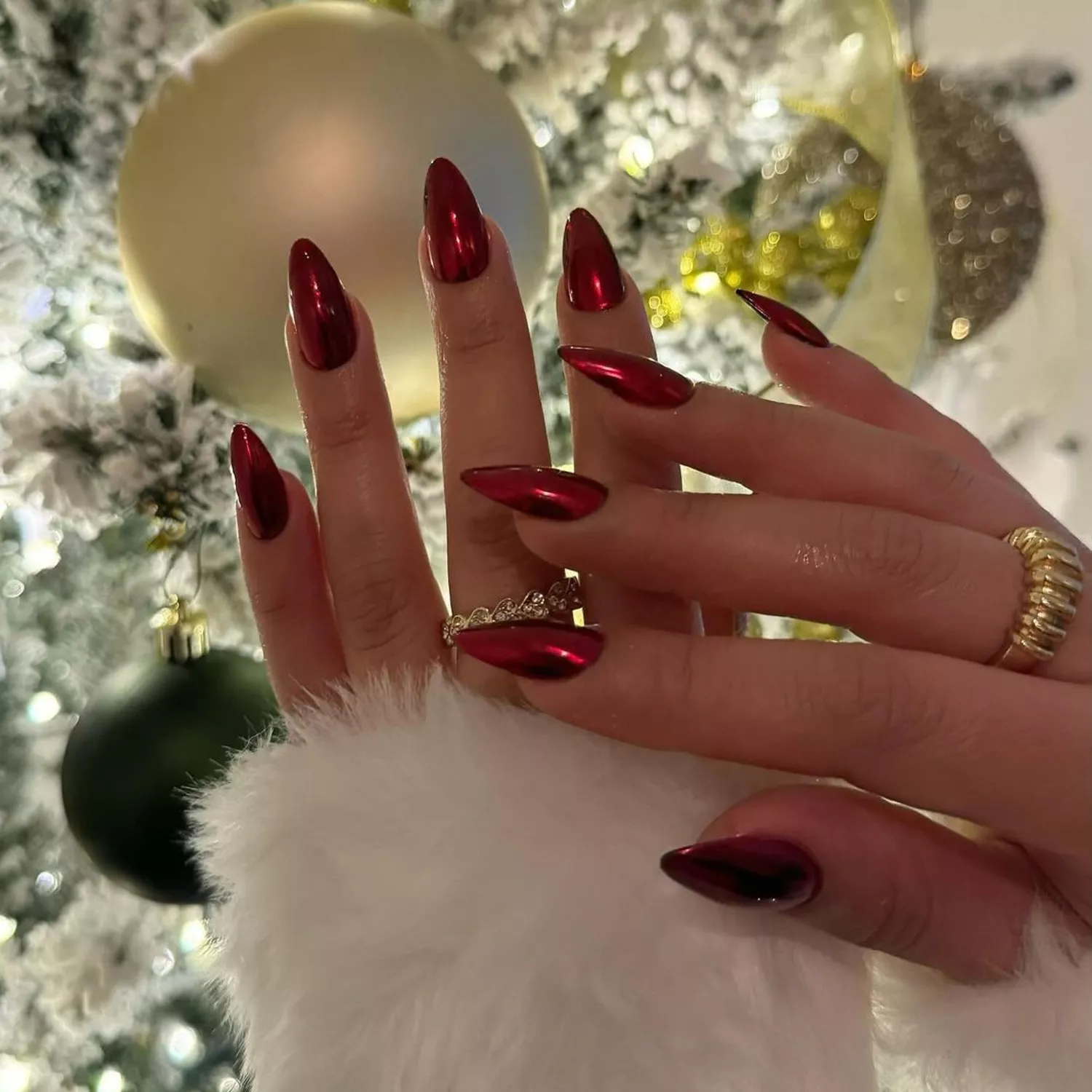 Person showing off their red chrome nails in front of a Christmas tree