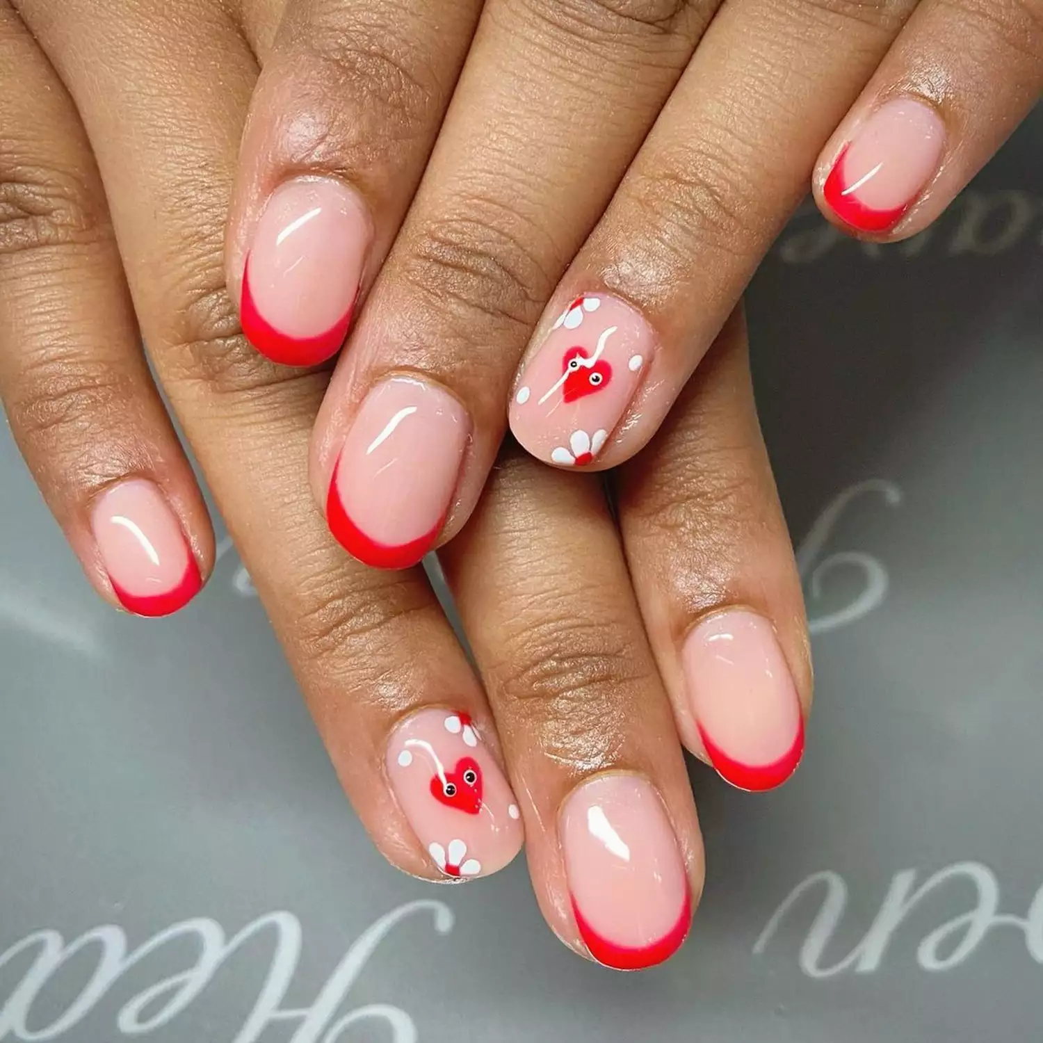 Person showing off their red French tips with heart accents on the ring finger nail