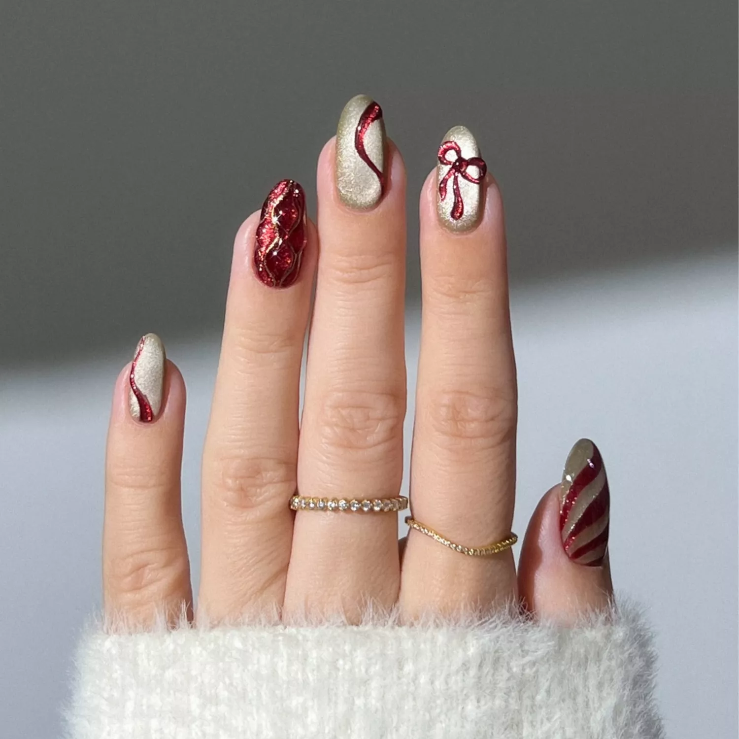 Velvet gold nails with maroon bow, swirl, and cable knit texture details.