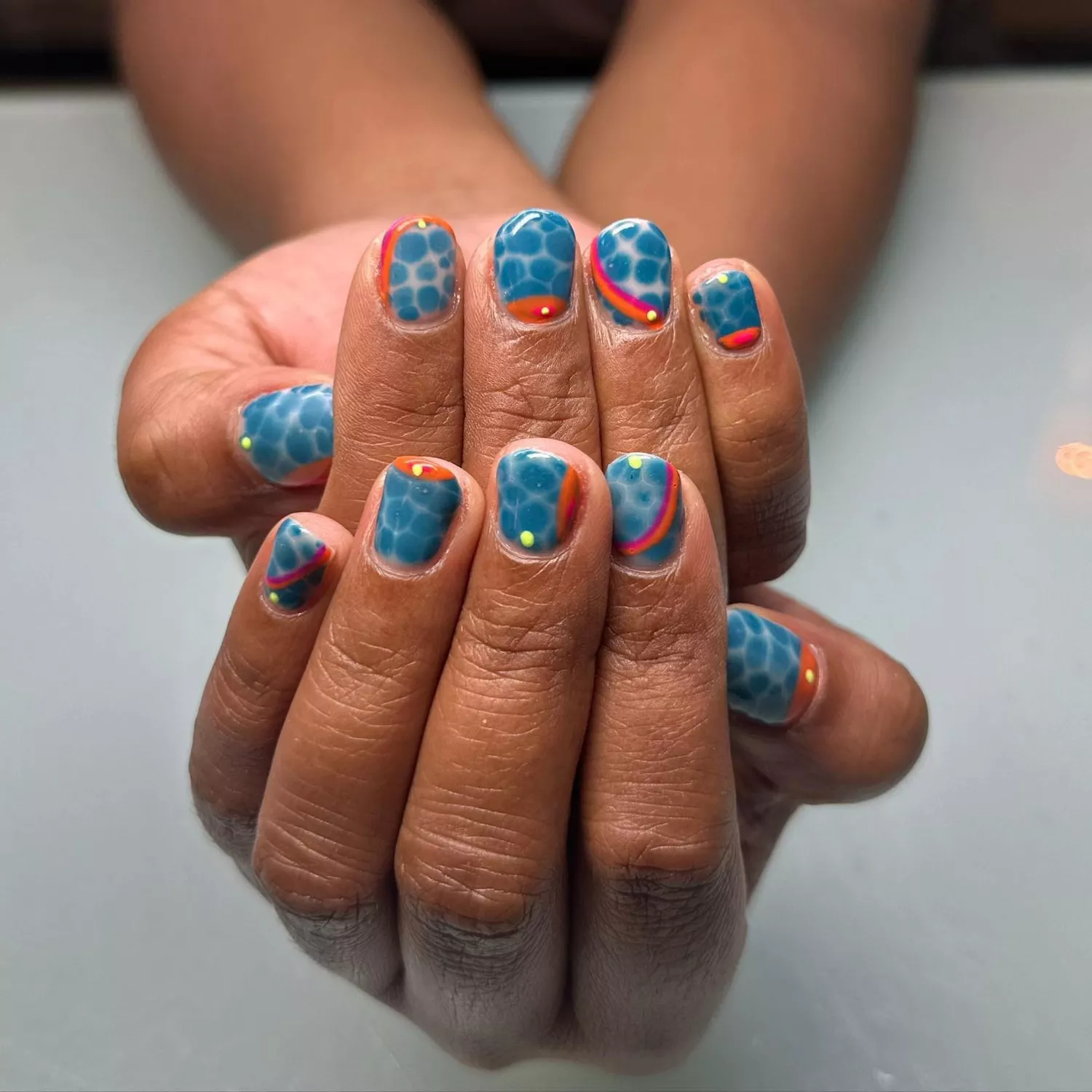 Pair of hands with nails that look like pool water with orange, pink, and yellow details